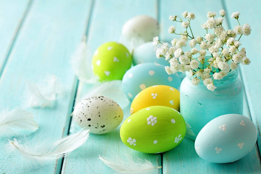 Ilustračná fotografia, na ktorej sú pomaľované veľkonočné vajíčka, vo váze sú kvety, pri vajíčkach sú pierka. 