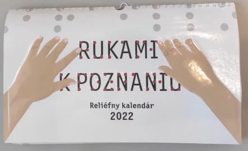 titulná strana reliéfneho nástenného kalendára rukami k poznaniu. Na obrázku je názov kalendára v umelecky zväčšenom braili a dve ženské ruky, ktoré názov čítajú