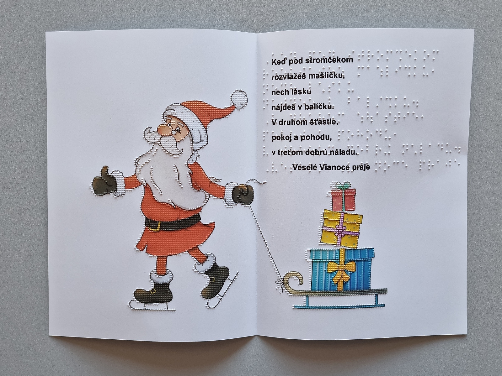Vianočná pohľadnica, na farebnom obrázku je vyobrazený Mikuláš v čiapke s brmbolcom. Mikuláš za sebou ťahá sane s darčekmi. Text v braili aj čiernotlači.